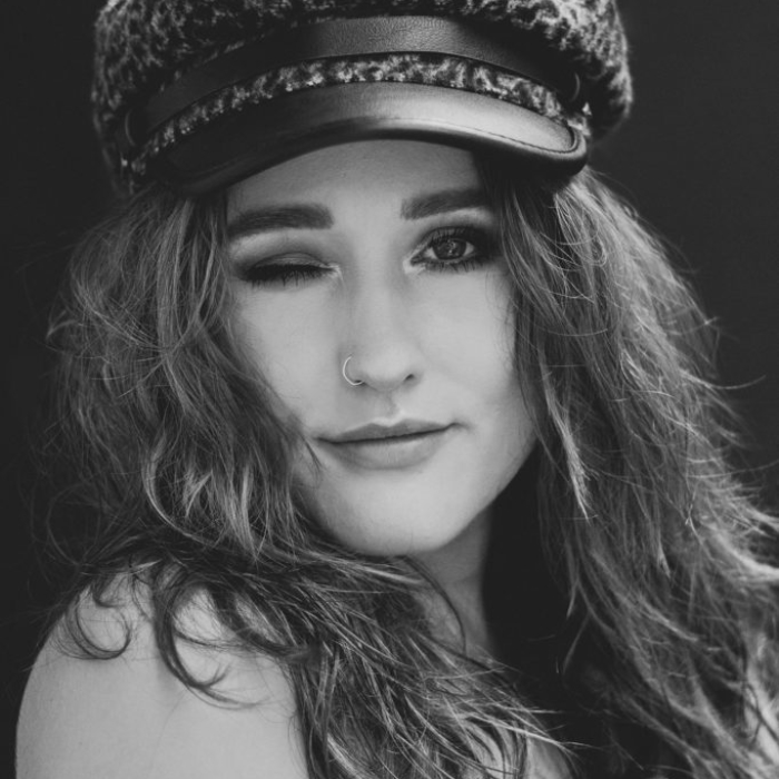 black and white image of pretty white girl with long hair in a baker boy hat winking and smiling