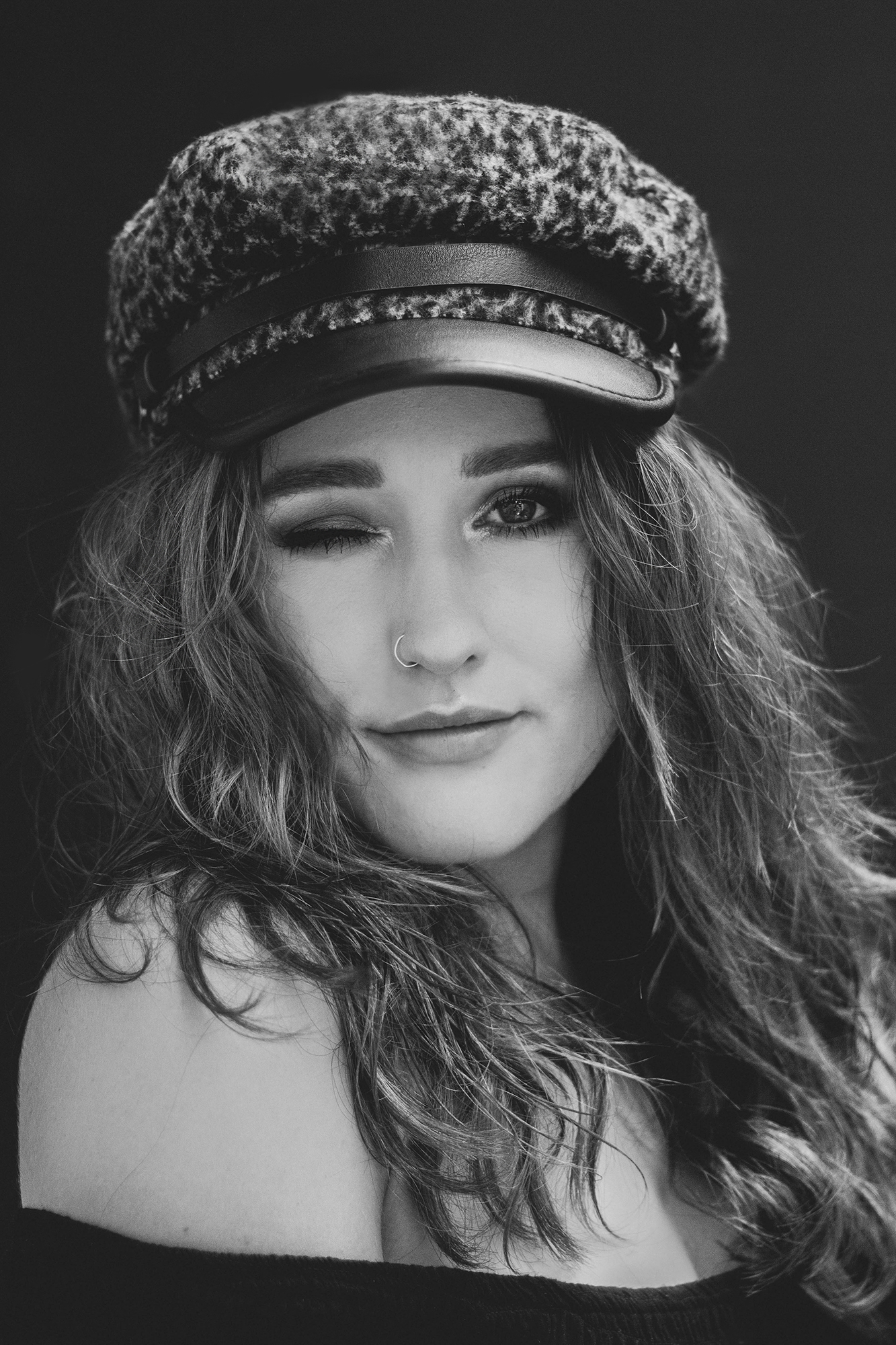 black and white image of pretty white girl with long hair in a baker boy hat winking and smiling