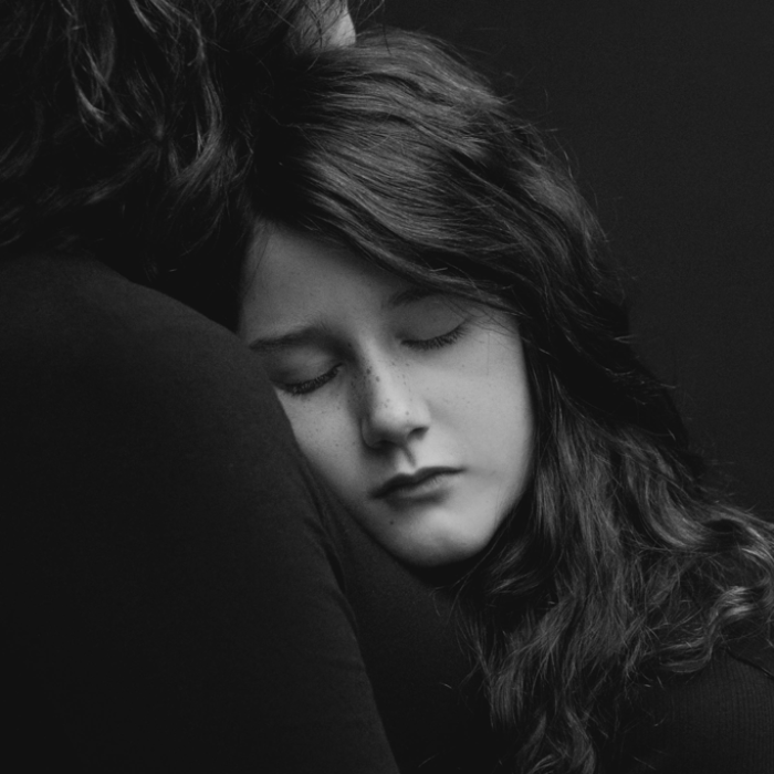 black and white image of young girl with eyes closed resting on her mother's chest