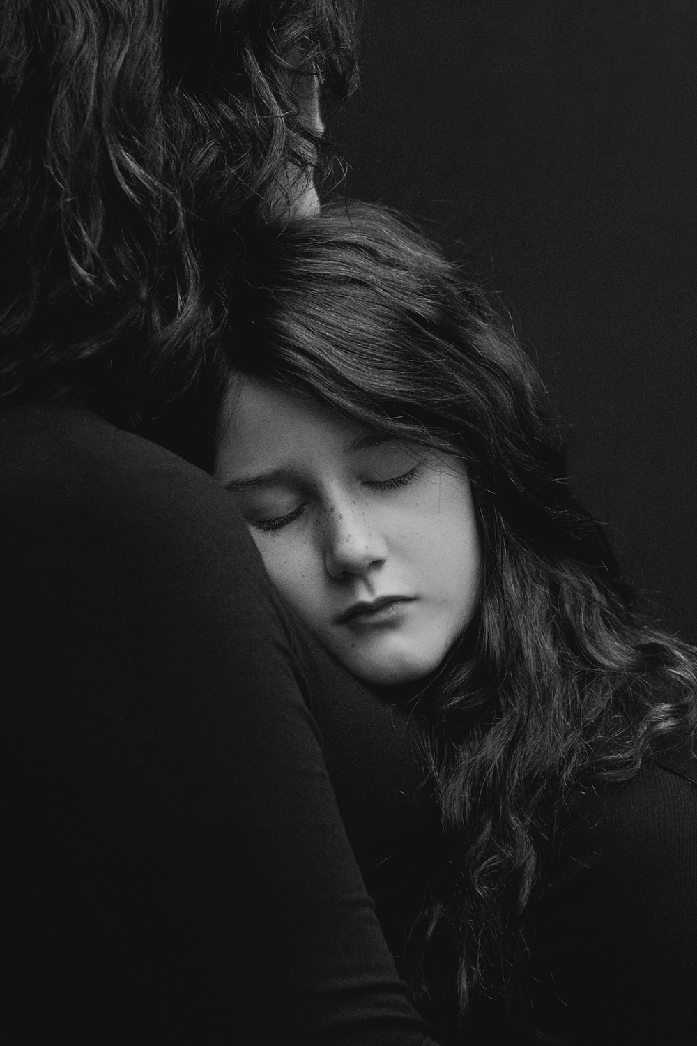 black and white image of young girl with eyes closed resting on her mother's chest