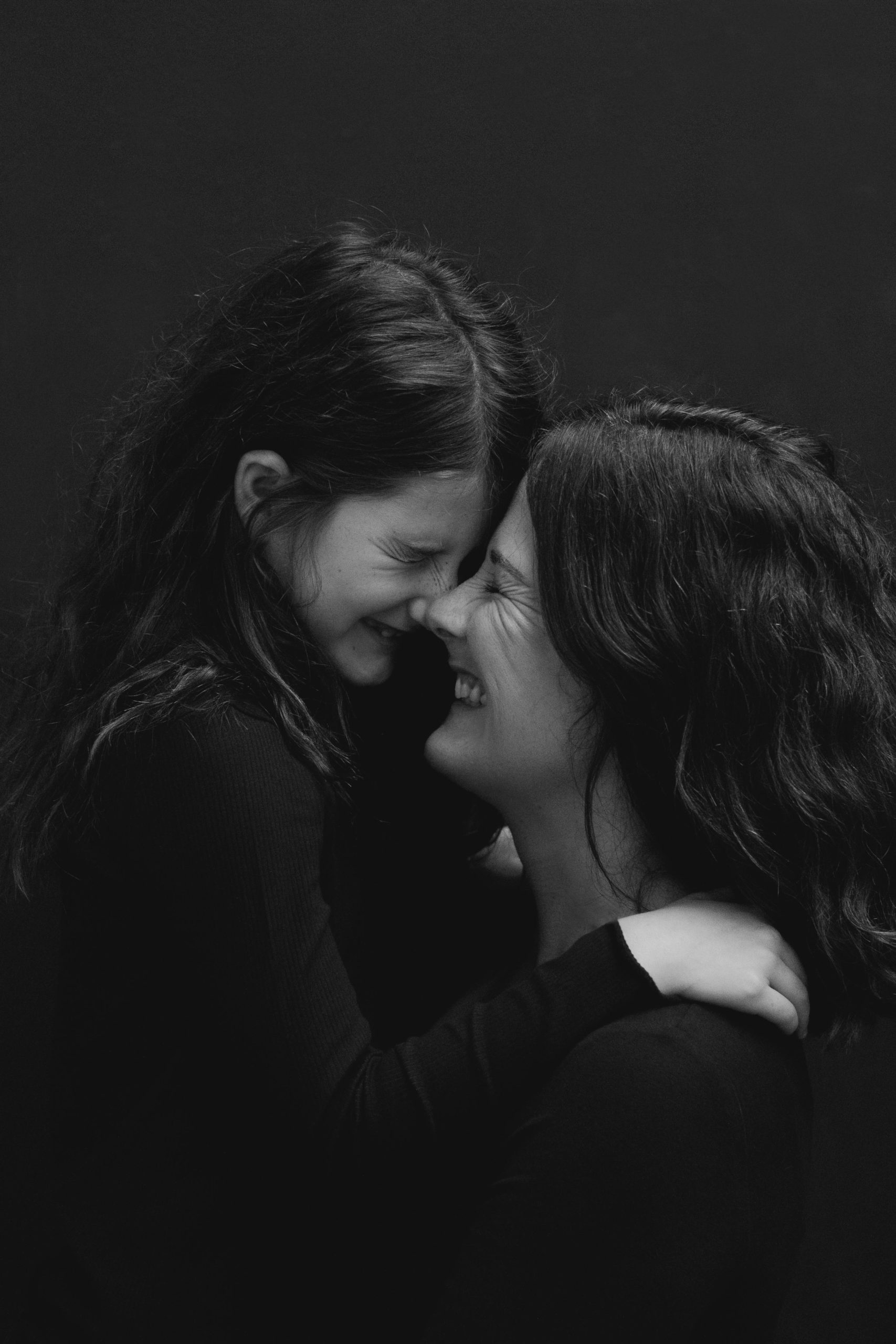 Black and white images of a young girl and mother laughing with noses touching
