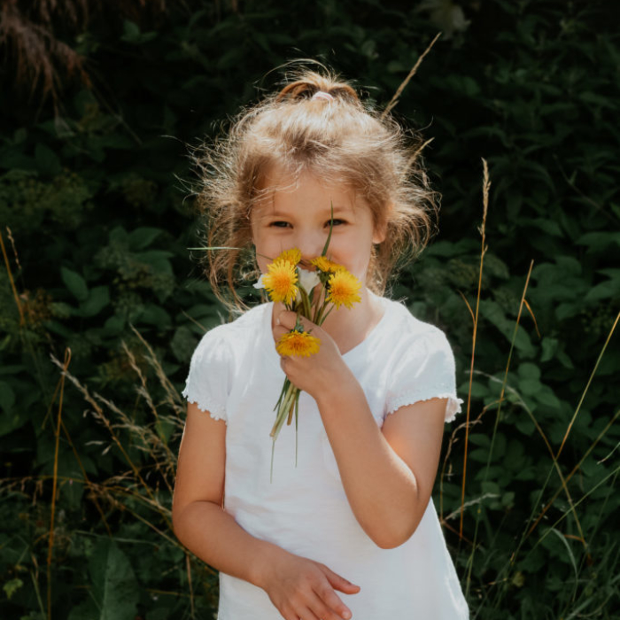 Young girl holding wild flowers up to face in a park