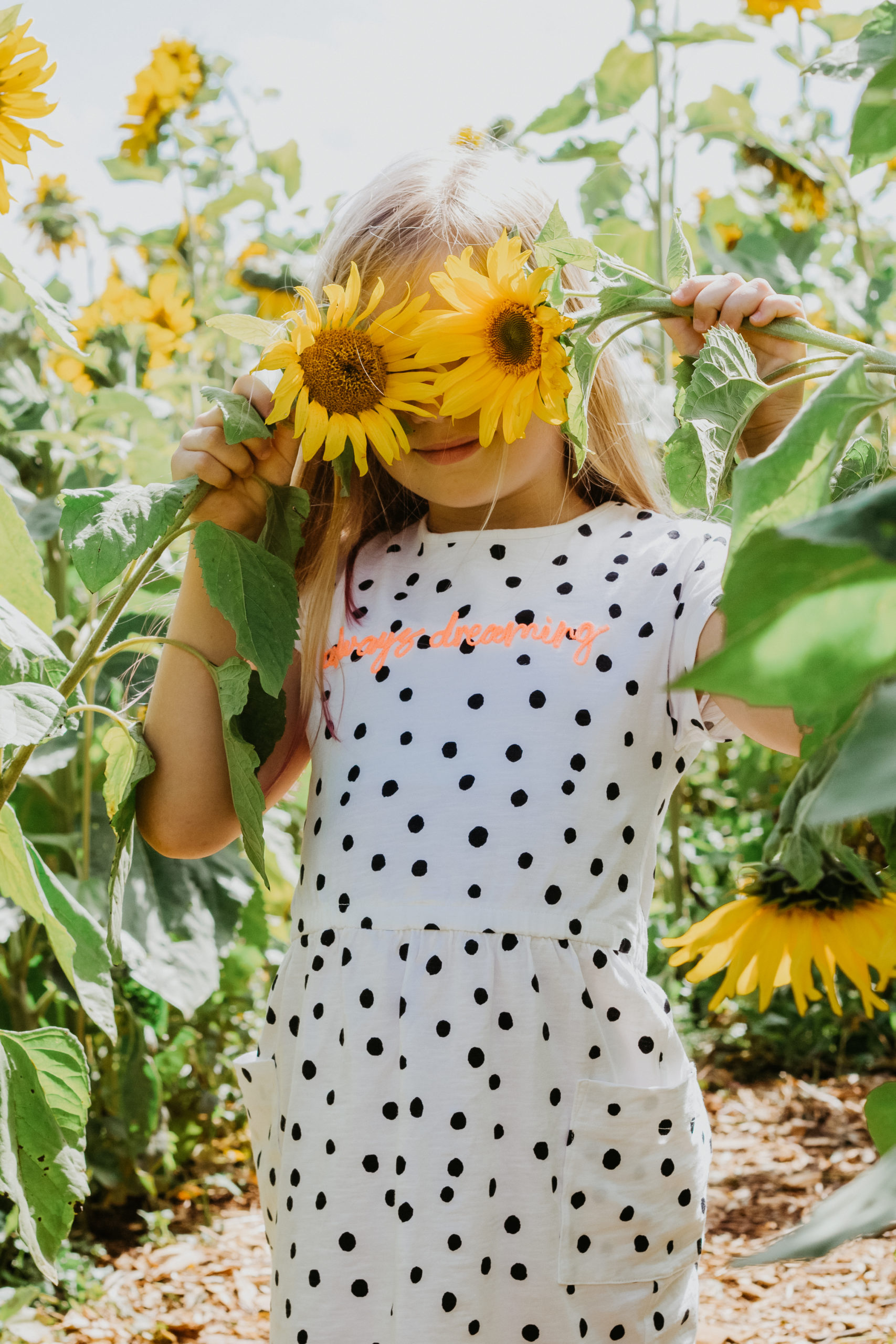 young blonde white girl holding sunflowers over eyes in black and white spotty dress