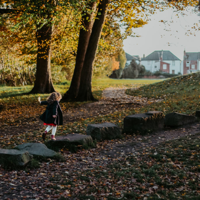 Young girl jumping on large rocks in a park whilst holding a leaf