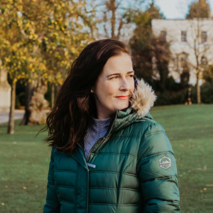 white woman with brunette hair in green puffer coat outside smiling in a park
