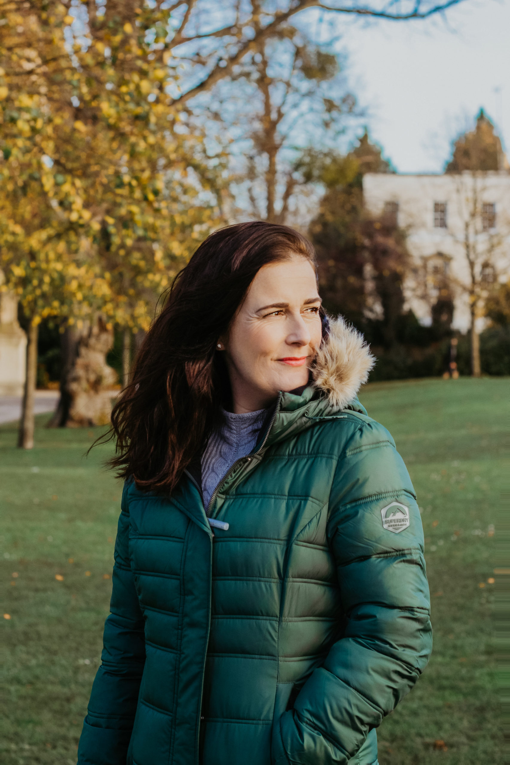 white woman with brunette hair in green puffer coat outside smiling in a park